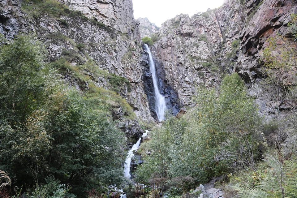 A tall waterfall dropping through a rocky gorge near Gveleti in the Kazbegi area, with trees in the foreground