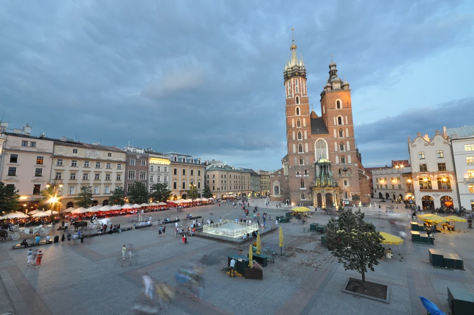 St. Mary's Basilica and the Main Market Square in Kraków at dusk, with café umbrellas and a lit fountain