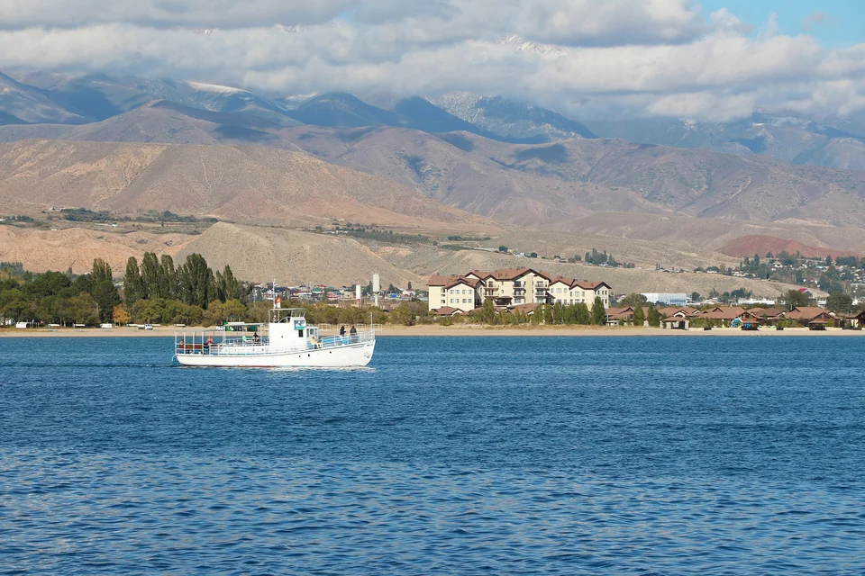Ein weißes Ausflugsboot auf dem blauen Wasser des Yssykköl bei Tscholpon-Ata, dahinter Berge