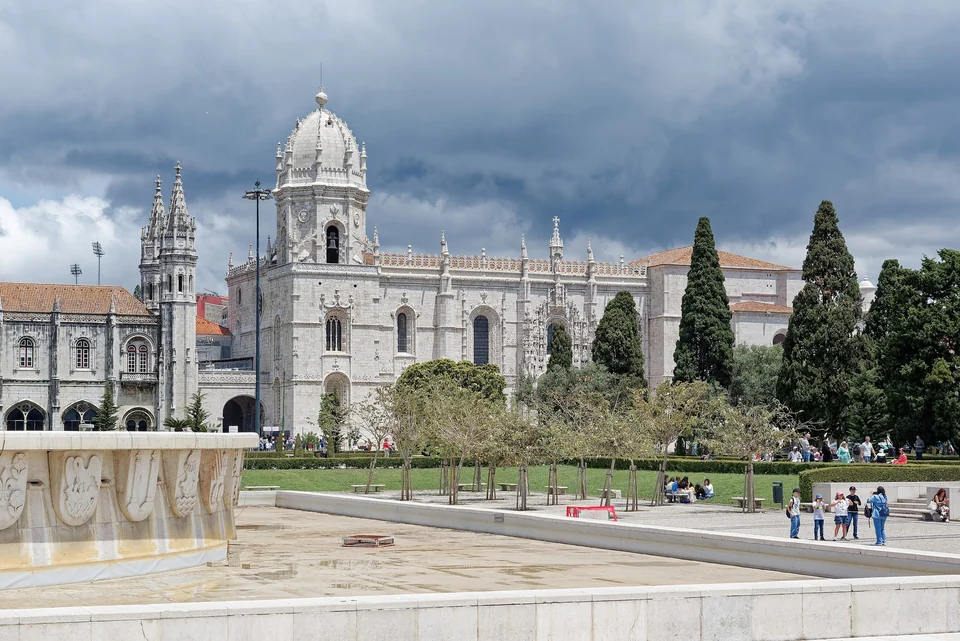 The long limestone facade and towers of the Jerónimos Monastery in Belém, Lisbon, behind a garden