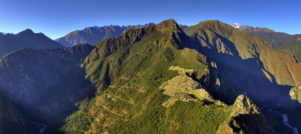Panoramic view of Machu Picchu terraces and stone buildings with green Andean peaks around the citadel in Peru