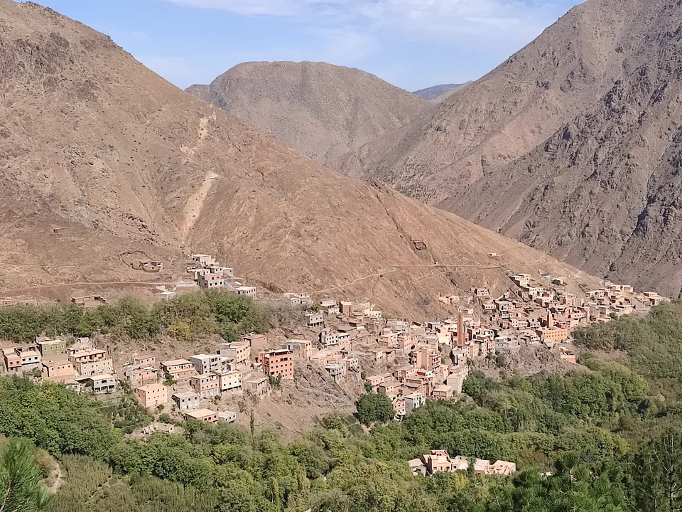 Earthen-colored houses of a village near Imlil spread across a green valley below the barren High Atlas mountains