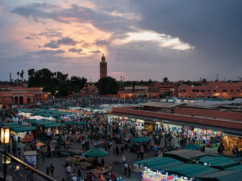 Jemaa el-Fnaa square in Marrakech at sunset, crowded with market stalls, with the Koutoubia minaret on the skyline