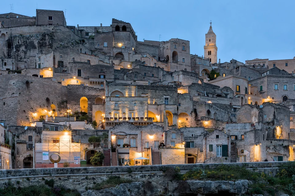 Sasso Barisano in Matera at blue hour with lit stone houses climbing the hillside toward the cathedral