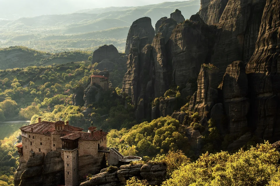 Le monastère de Roussanou sur son rocher au-dessus de collines verdoyantes, avec les piliers des Météores qui se dressent derrière, en Grèce