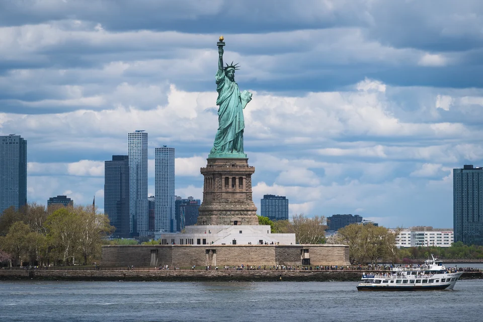 The Statue of Liberty on Liberty Island with a sightseeing boat passing in the harbor, New York