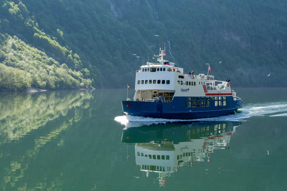 Eine Fähre fährt unter steilen grünen Wänden durch den Nærøyfjord in Norwegen