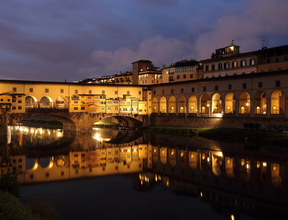 Ponte Vecchio bridge with shops built along it, reflected in the Arno River at dusk in Florence, Italy