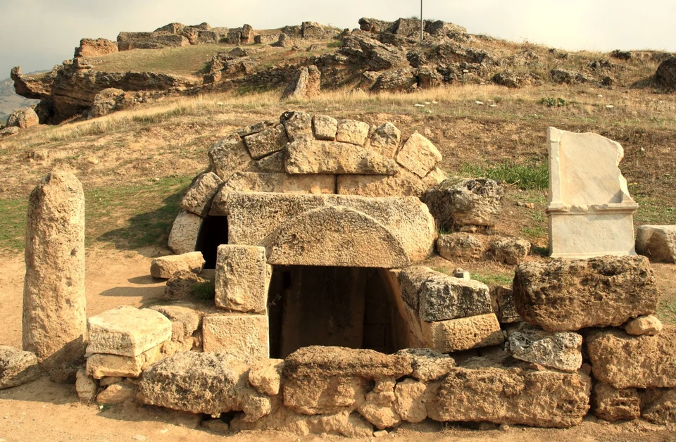A vaulted stone tomb in the Necropolis of Hierapolis with ruins on the hill behind