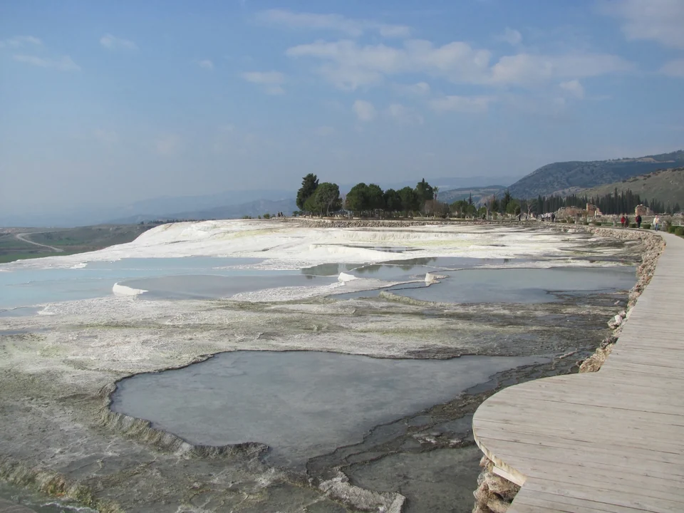 Pale travertine pools and a wooden walkway along the edge of the terraces at Pamukkale, Türkiye
