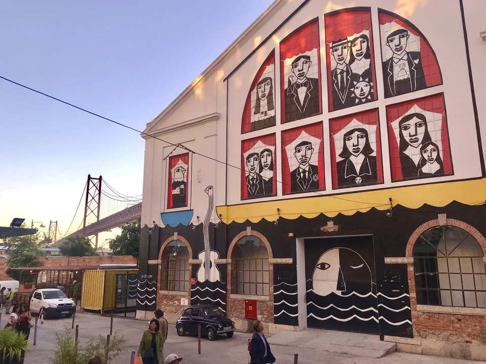 Painted former factory building at LX Factory in Alcântara, Lisbon, with the 25 de Abril Bridge behind