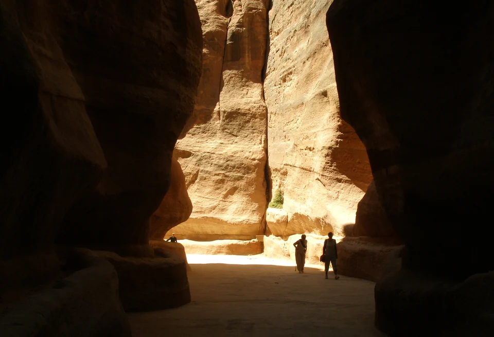 Visitors walking through the narrow, shadowed sandstone gorge of the Siq leading into Petra, Jordan