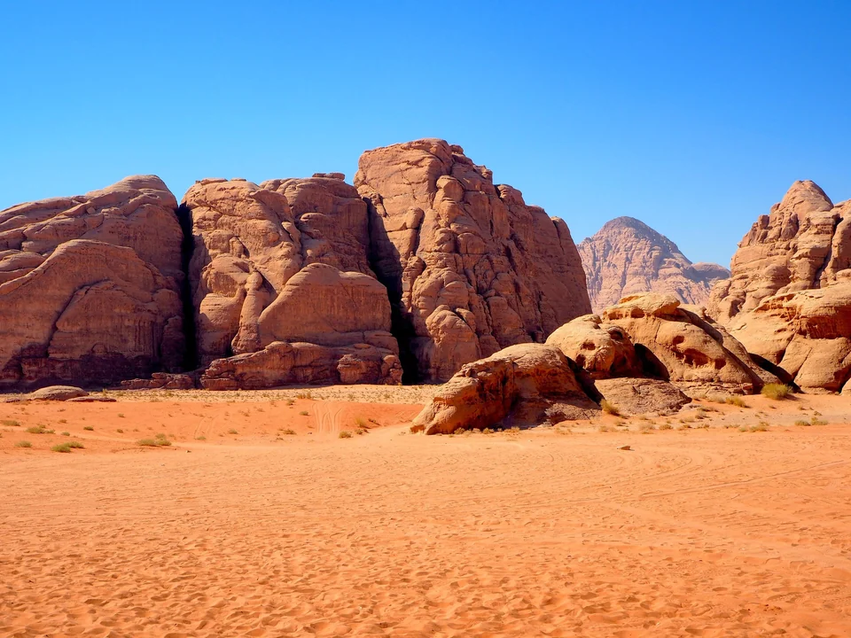 Weathered sandstone mountains rising from orange sand under a deep blue sky in Wadi Rum, Jordan