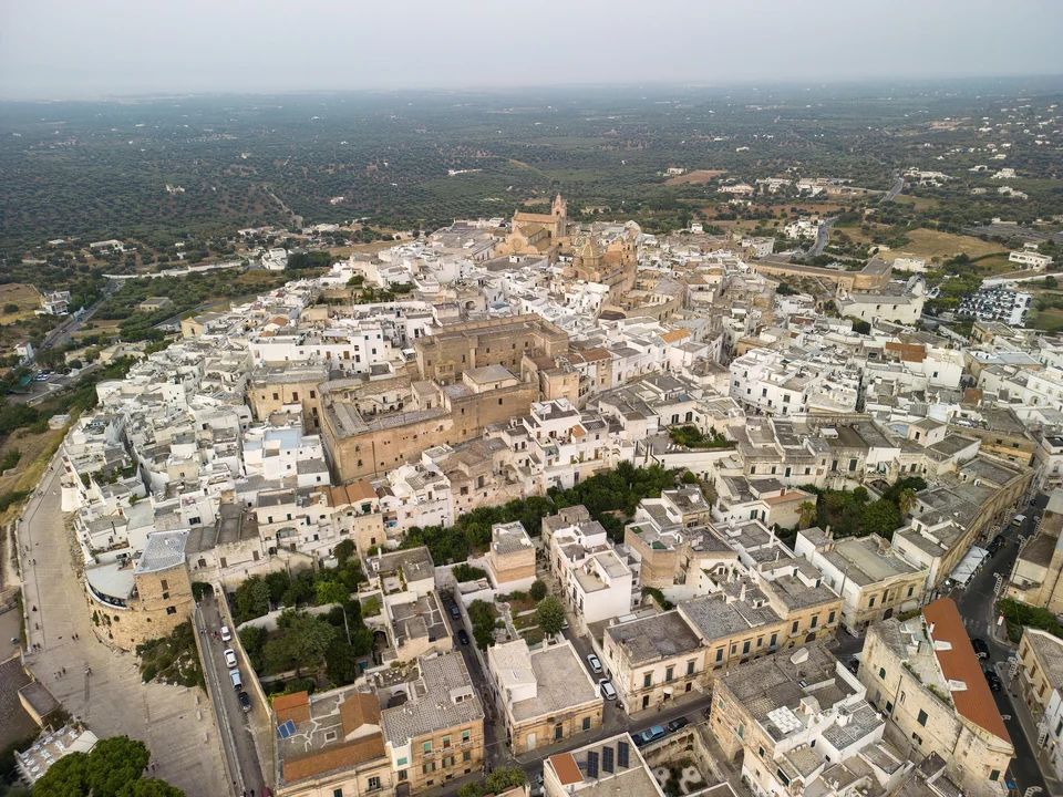 Aerial view of Ostuni's whitewashed old town on its hilltop, with the cathedral and olive groves around it