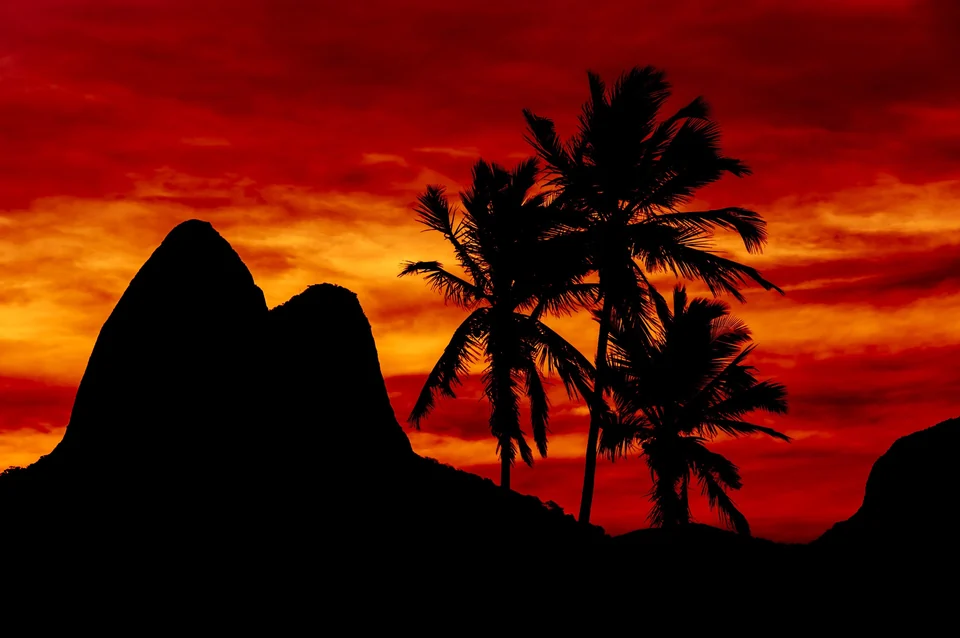 Red sunset over Ipanema beach with palm trees and the Dois Irmãos mountain silhouetted in Rio de Janeiro