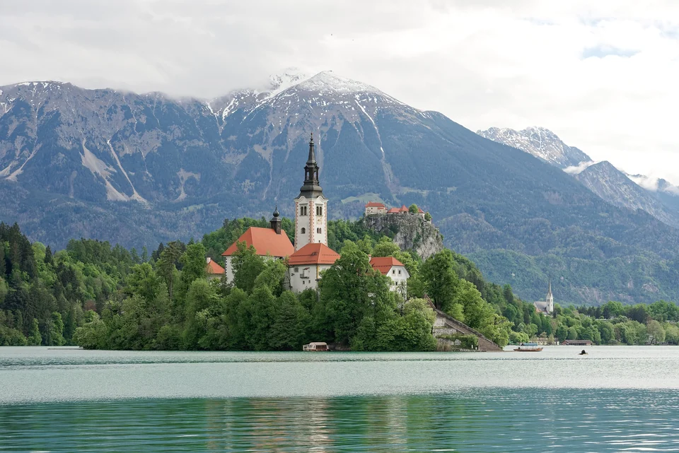 Bled Island with its white church tower on Lake Bled, Bled Castle on the cliff behind and the Julian Alps beyond