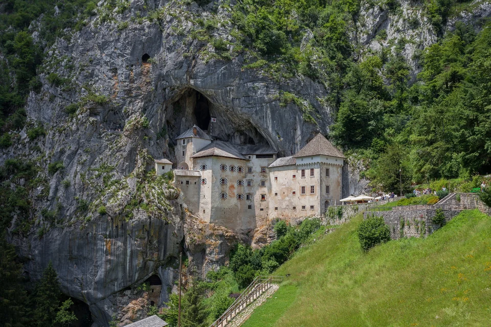 Predjama Castle's white Renaissance facade built into a cave opening in a tall limestone cliff in Slovenia