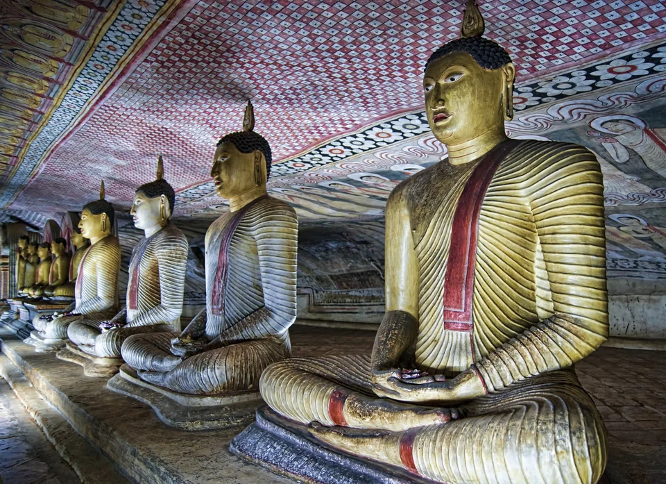 Rows of painted seated Buddha statues beneath murals inside a Dambulla cave temple in Sri Lanka