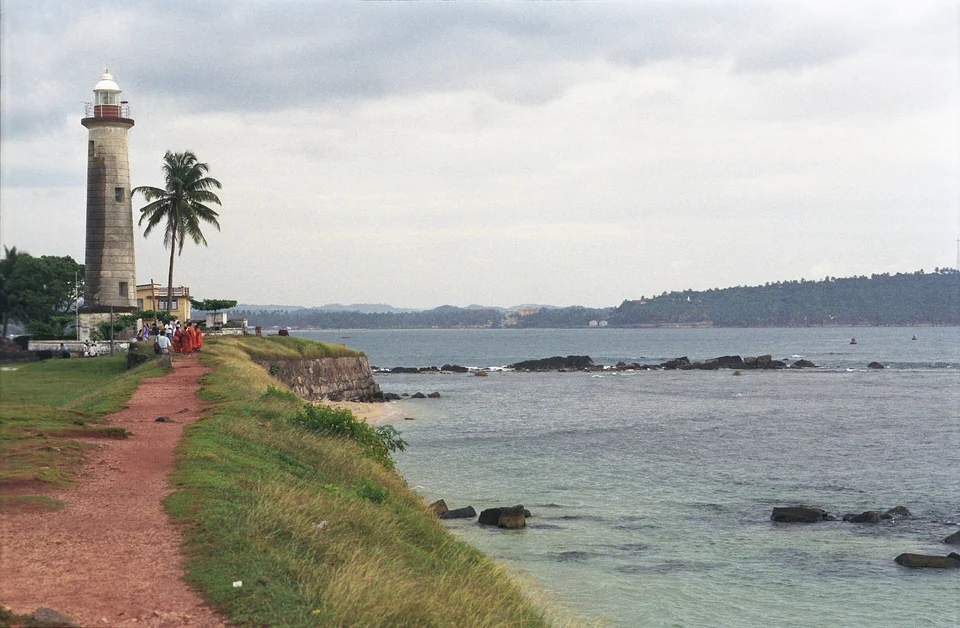 White lighthouse on the ramparts of Galle Fort with palm trees and the Indian Ocean, Sri Lanka