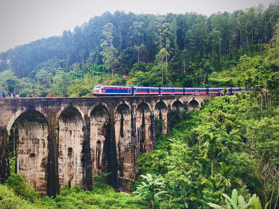 Blue passenger train crossing the stone Nine Arch Bridge surrounded by thick forest near Ella, Sri Lanka