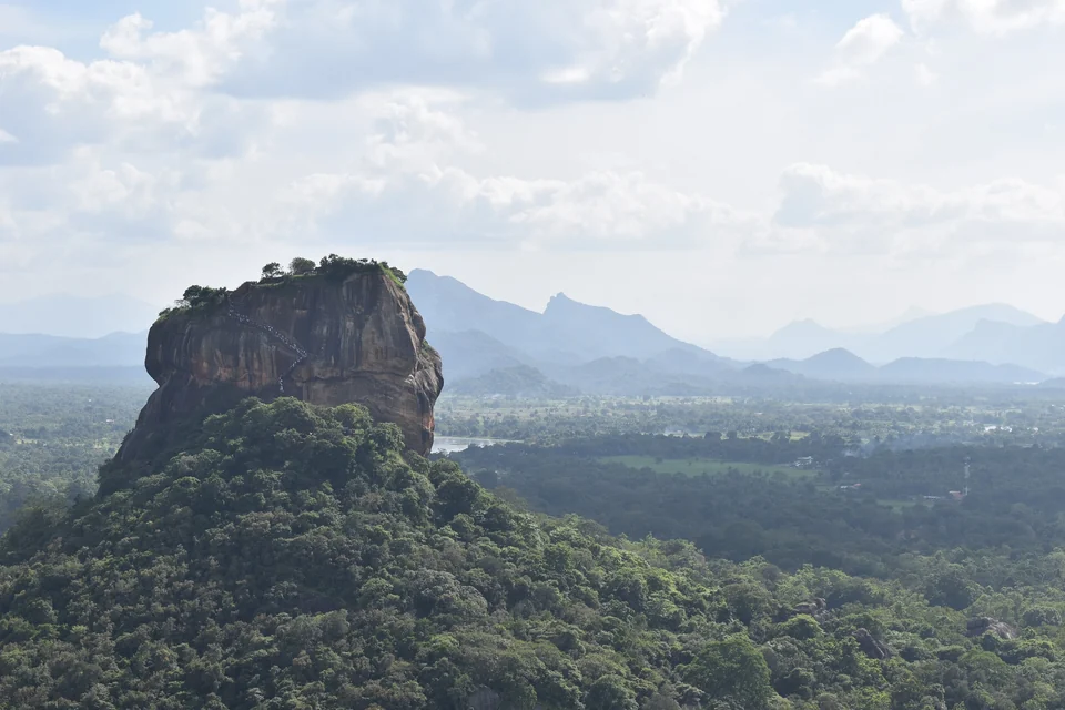 Sigiriya Rock Fortress rising above green forest and distant hills, seen from Pidurangala Rock in Sri Lanka