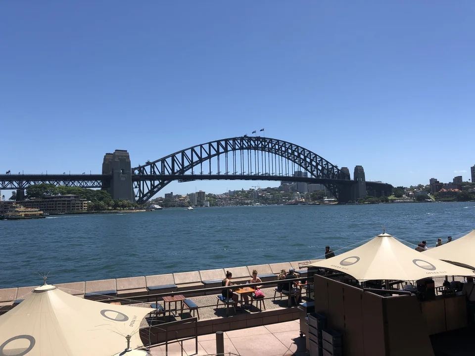 Sydney Harbour Bridge across blue water on a clear day, seen from a waterfront terrace at Circular Quay