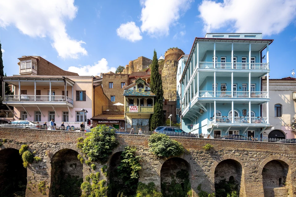Balconied houses above the brick arches of Abanotubani in Old Tbilisi, with Narikala fortress walls rising behind