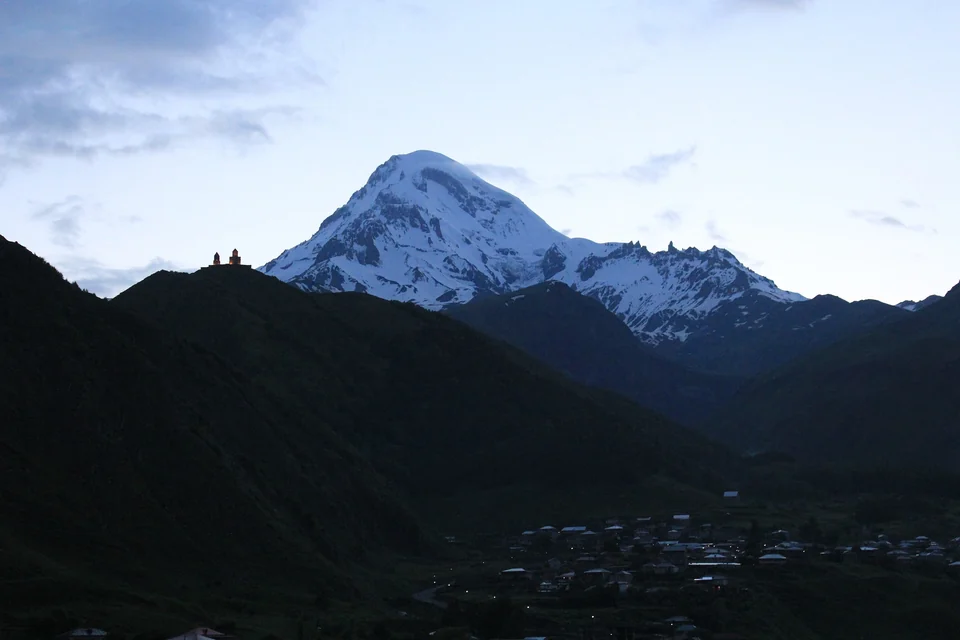 Snow-covered Mount Kazbek at dusk with the small Gergeti Trinity Church on a dark ridge above Stepantsminda
