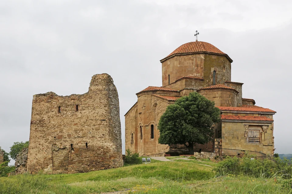 Stone Jvari Monastery with a red-tiled dome beside a ruined tower on a grassy hilltop above Mtskheta, Georgia