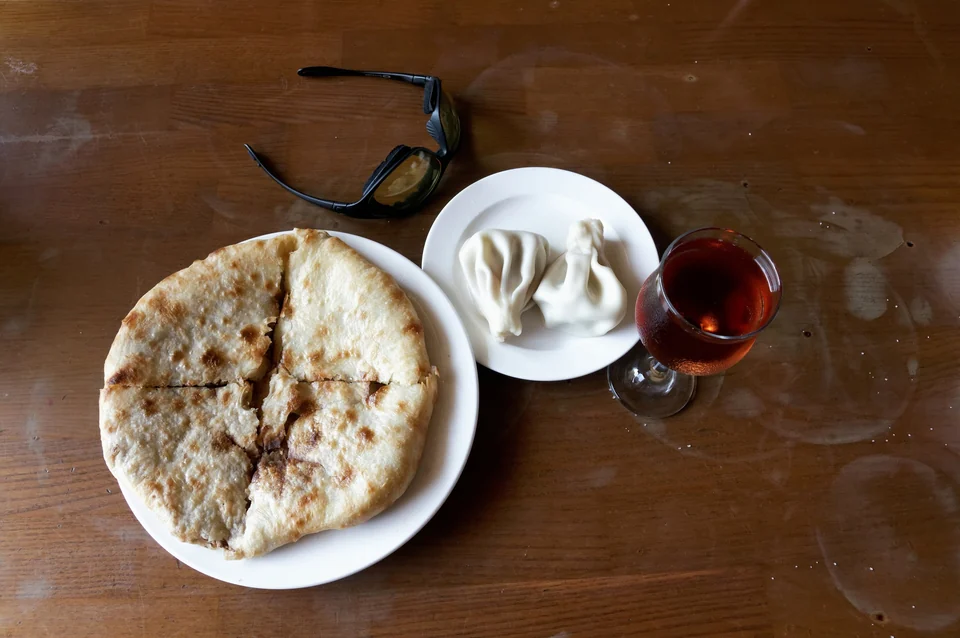A round khachapuri cheese bread, two khinkali dumplings and a glass of red wine on a wooden table in Tbilisi