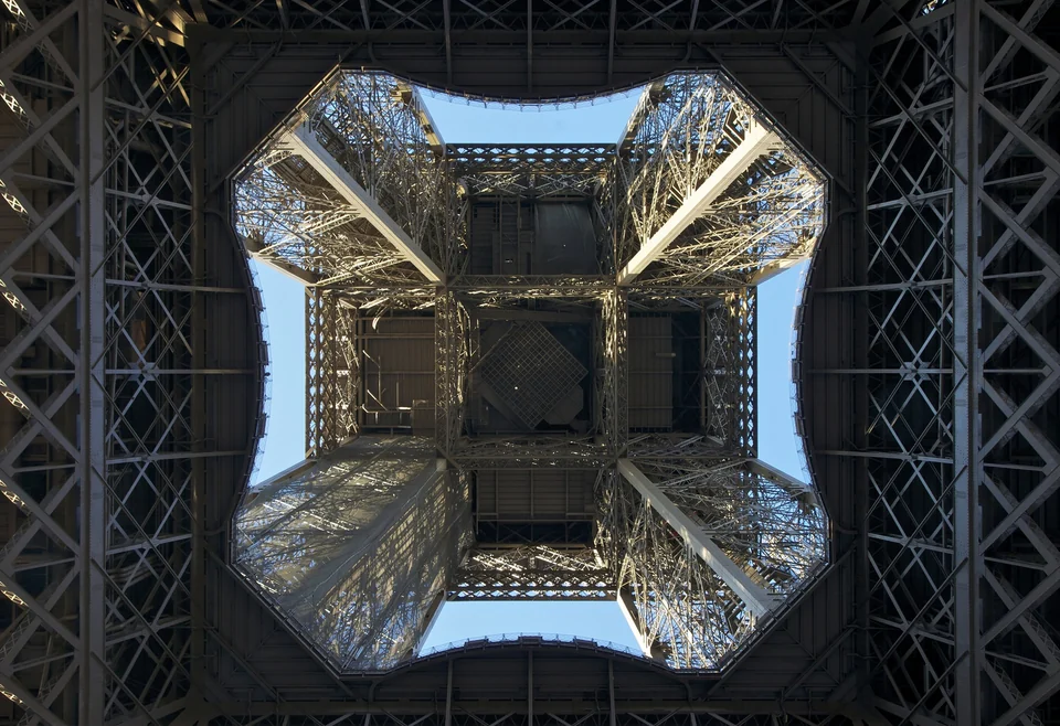 View straight up through the iron lattice of the Eiffel Tower from the square beneath its four legs
