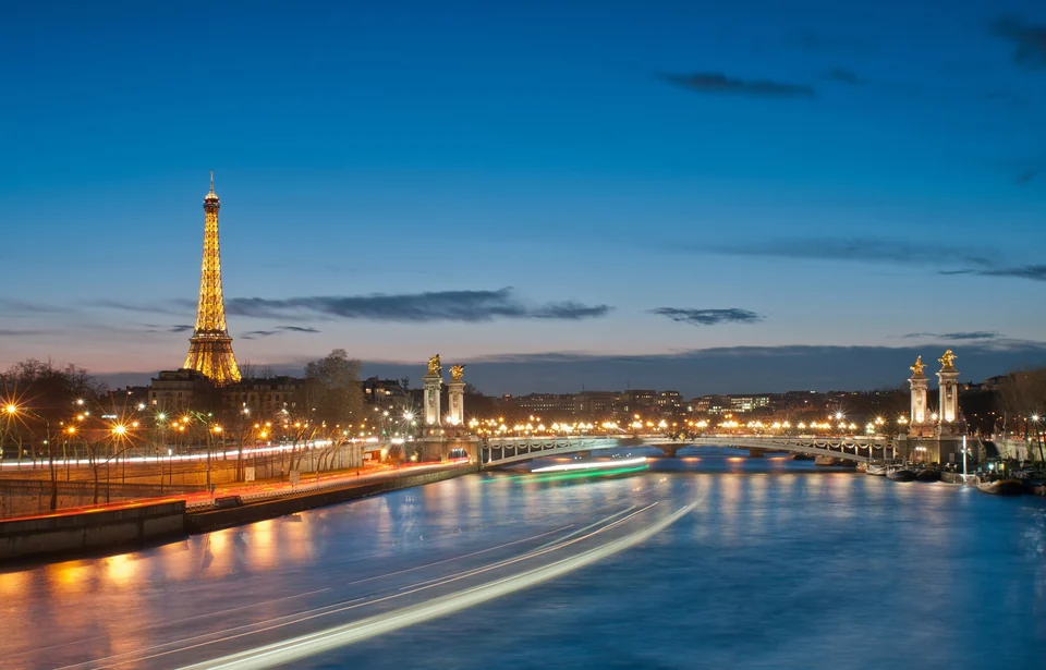The illuminated Eiffel Tower at dusk seen along the Seine with the lamps of Pont Alexandre III in Paris
