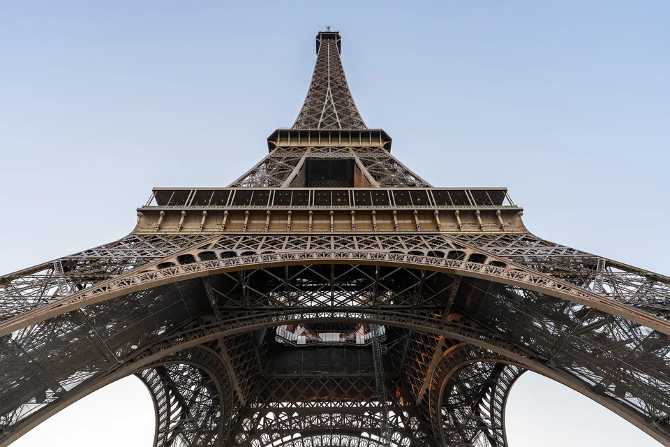 Close view of the Eiffel Tower's iron lattice and first-floor arch against a pale sky