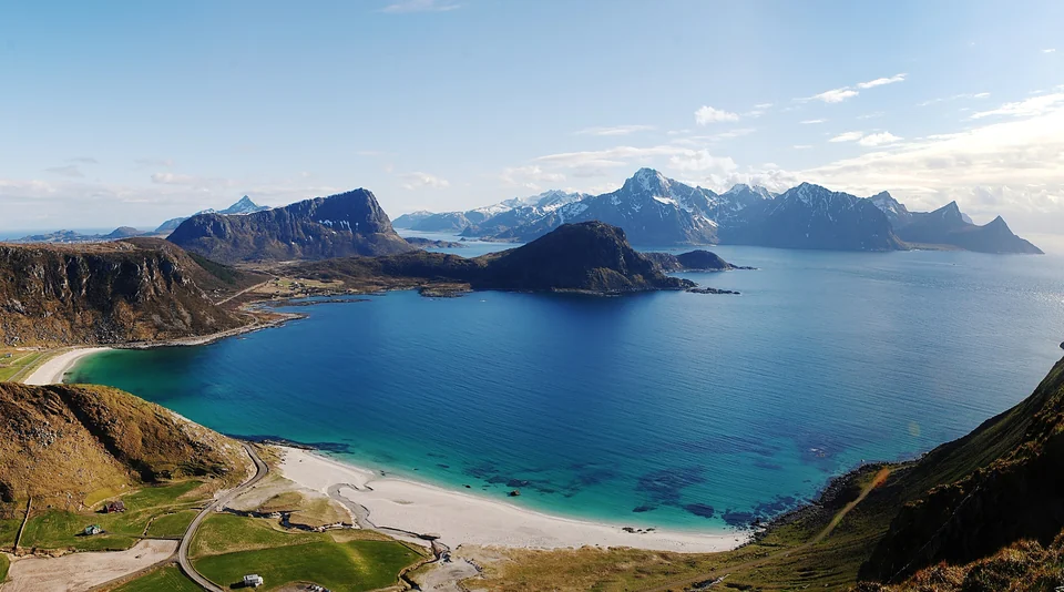 Turquoise bay and white sand of Haukland Beach seen from above, with Lofoten mountains across the water in Norway