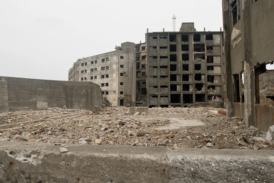 Crumbling multi-story concrete apartment blocks and rubble seen from the tour route on Hashima Island