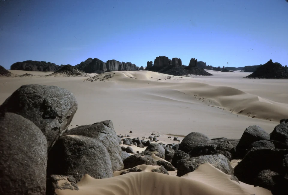 Dark sandstone rock towers rising from pale sand dunes on the edge of the Tassili n’Ajjer near Djanet, Algeria
