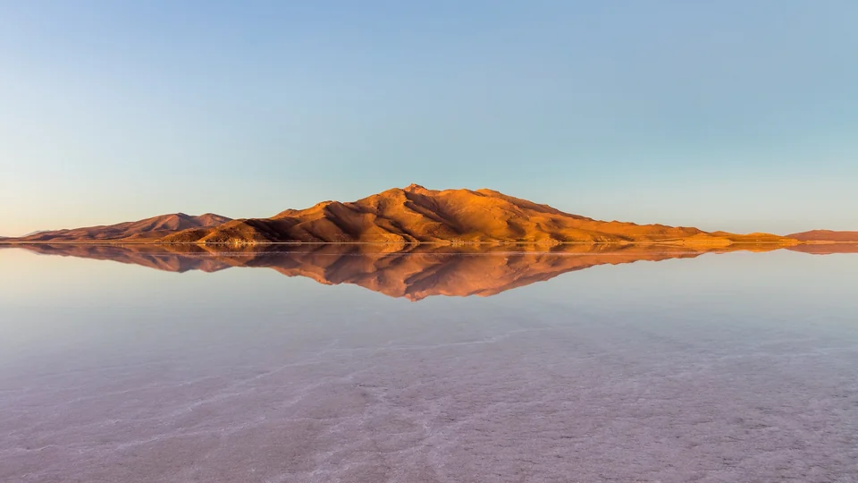 Mountains reflected in a thin layer of water on the Salar de Uyuni salt flat at sunrise, Bolivia