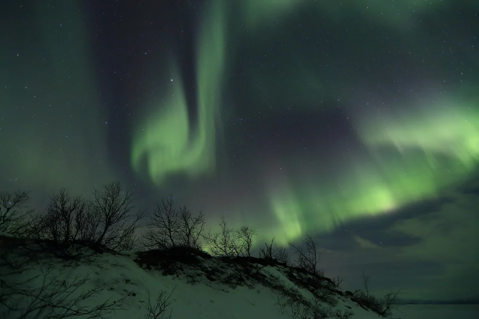Green northern lights over frozen Lake Torneträsk and mountains in Abisko National Park, Swedish Lapland