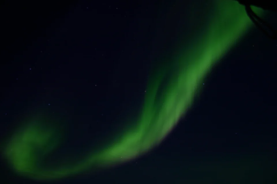 Green aurora borealis over snowy hills and scattered lights at Kangerlussuaq in West Greenland