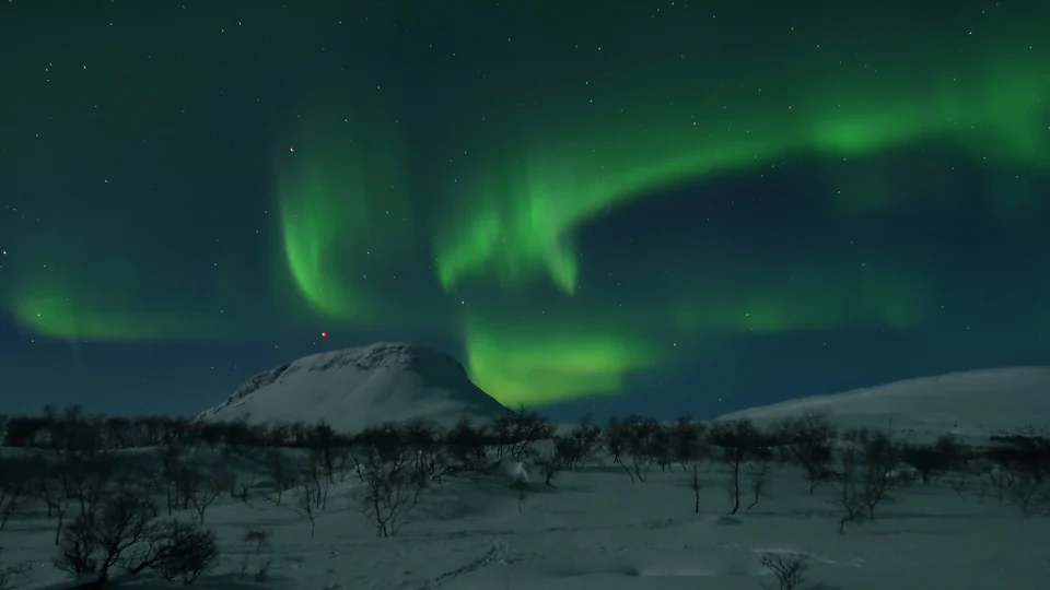 Northern lights arching over the snow-covered Saana fell in Kilpisjärvi, Finnish Lapland