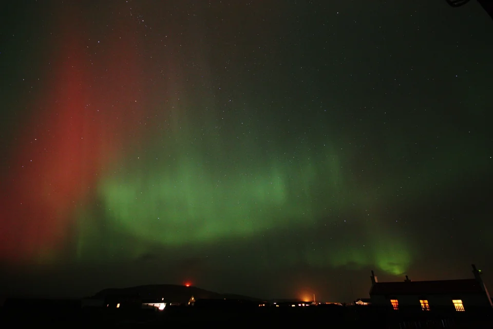 Green and red aurora above Fitful Head and an old stone house on the south coast of Shetland, Scotland