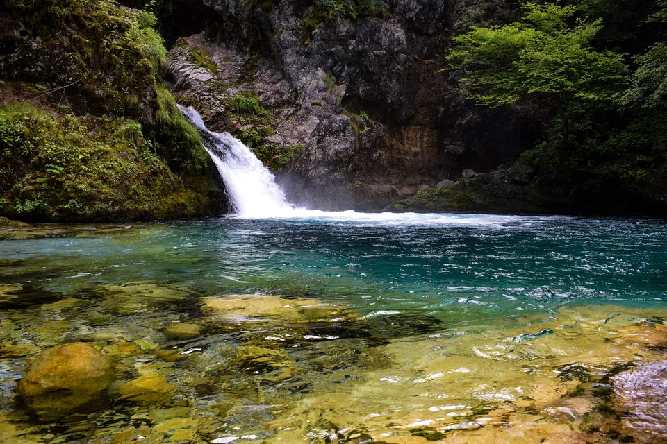 A small waterfall falling into the clear turquoise pool known as the Blue Eye of Theth in Albania
