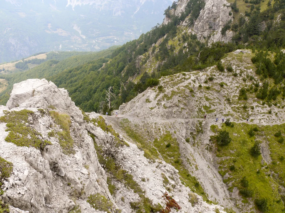 Hikers on the stony path below Valbona Pass with forested valleys falling away in the Albanian Alps