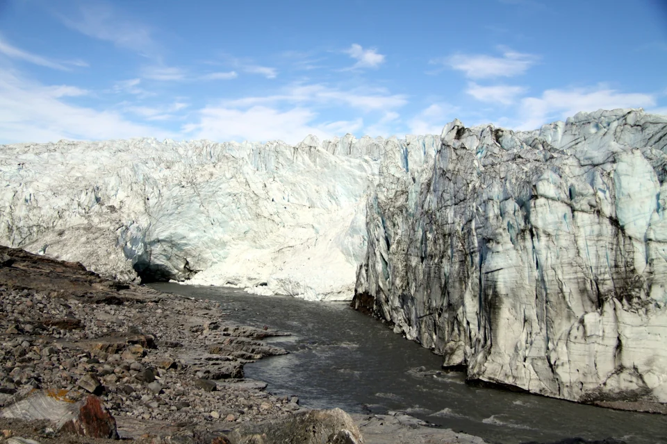 Tall cracked ice wall of Russell Glacier beside a gray meltwater river near Kangerlussuaq, Greenland