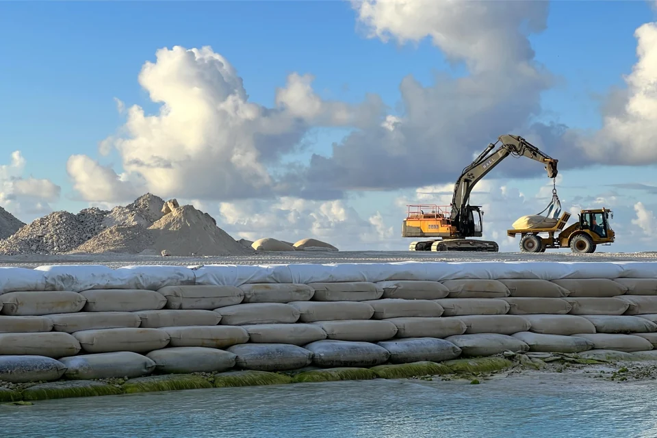 Excavator working on raised reclaimed land protected by a sandbag seawall on Funafuti, Tuvalu, in 2025