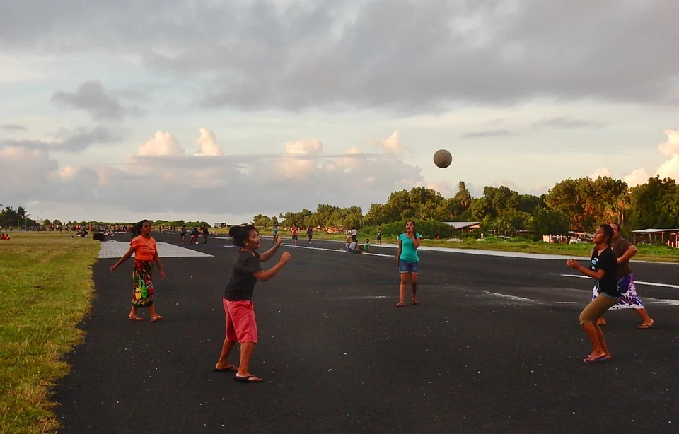 Young women playing volleyball on the runway of Funafuti International Airport at sunset, Tuvalu