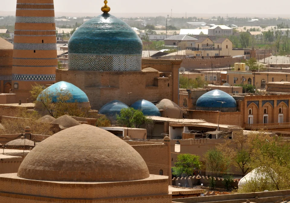 Turquoise and blue domes and a striped minaret seen over the rooftops of Itchan Kala in Khiva