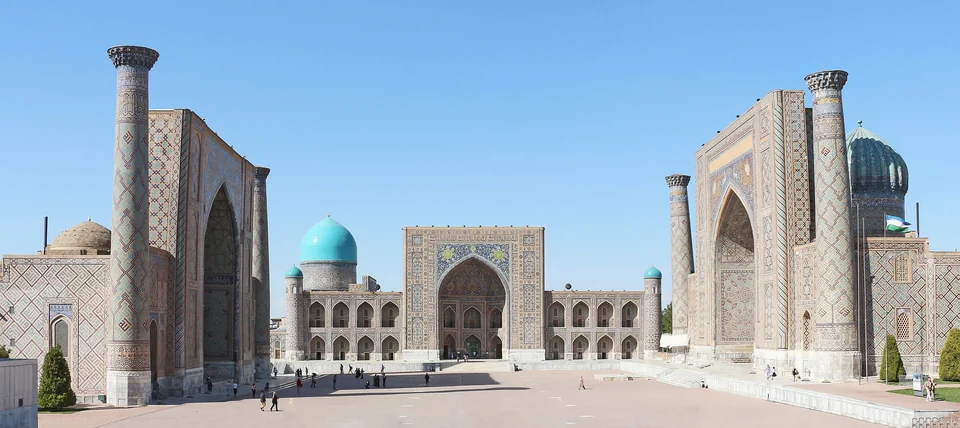 The three tiled madrasas of the Registan in Samarkand under a clear blue sky, with turquoise domes behind