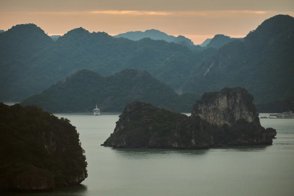 Forested limestone karst islands rising from calm water in Ha Long Bay, northern Vietnam, at dusk