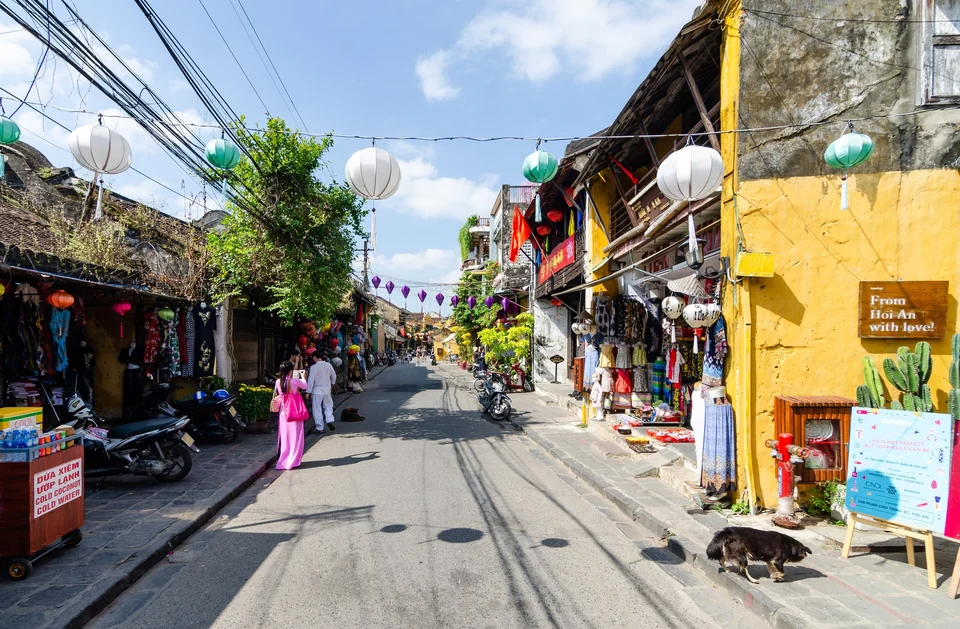 Yellow shophouses, clothing shops and silk lanterns strung over a street in Hoi An Ancient Town